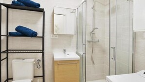 Une salle de bain moderne avec une douche à parois de verre, un lavabo blanc et des toilettes. On y trouve des étagères avec des serviettes et un miroir au-dessus du lavabo.