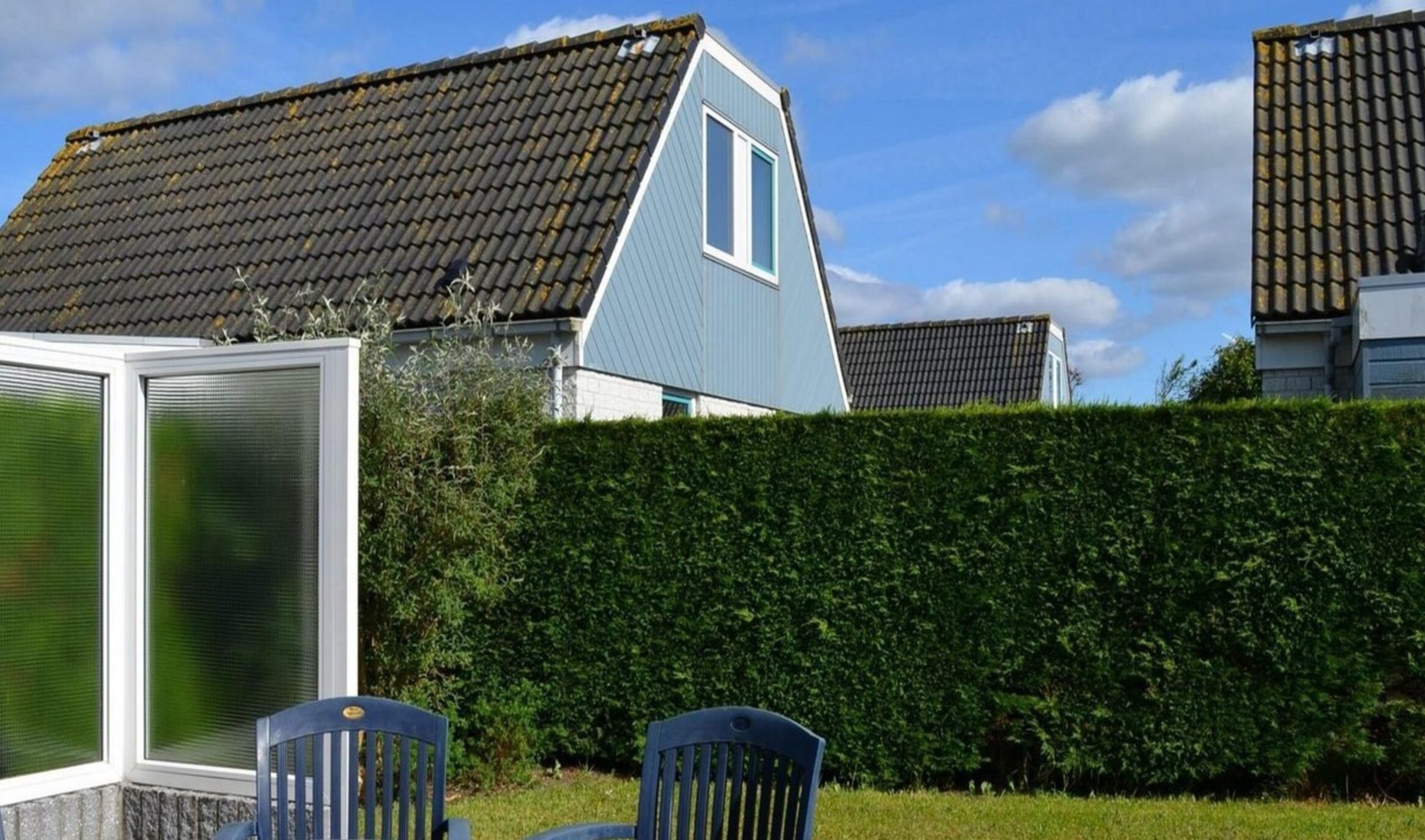 A residential area with houses featuring sloped roofs and a well-maintained hedge.