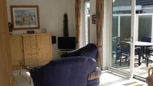 Un soggiorno con divano, televisore, mobiletti in legno e un'area pranzo con sedie e tavolo.