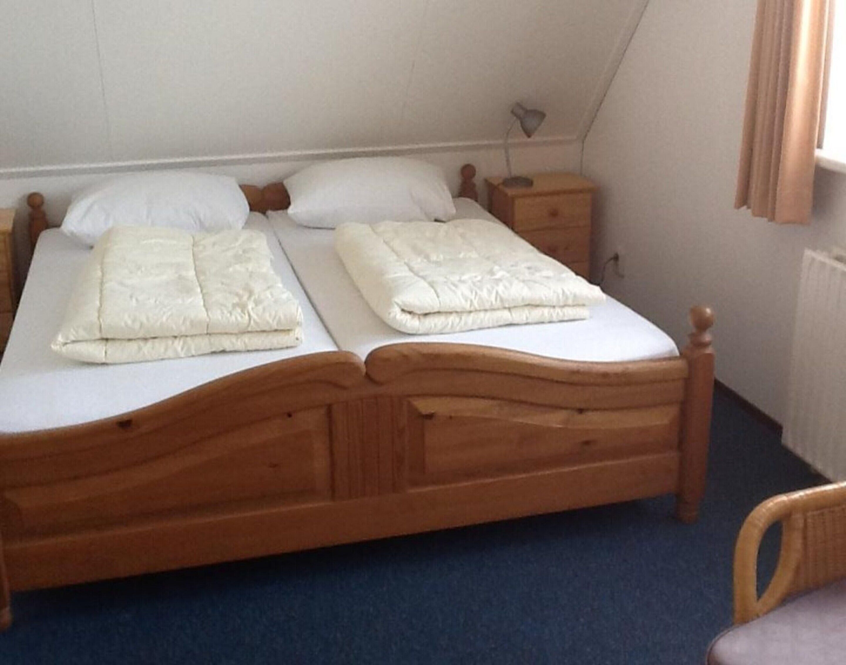 A single bed with a wooden frame and white bedding in a room with a blue carpet.
