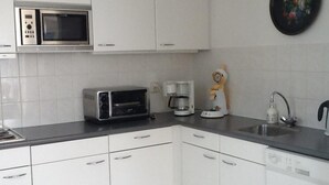 Una cucina con mobili bianchi, un forno a microonde, un tostapane, una macchina per il caffè e un lavandino.