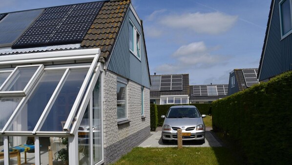 Ein Wohngebiet mit Häusern, die mit Solaranlagen ausgestattet sind, einem Auto auf der Einfahrt und einem gepflegten Rasen.