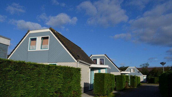 A row of modern, two-story houses with pitched roofs and blue exteriors, surrounded by well-maintained hedges. - Bungalow for 6 People, Near the Beach (Sint Maartensvlotbrug)
