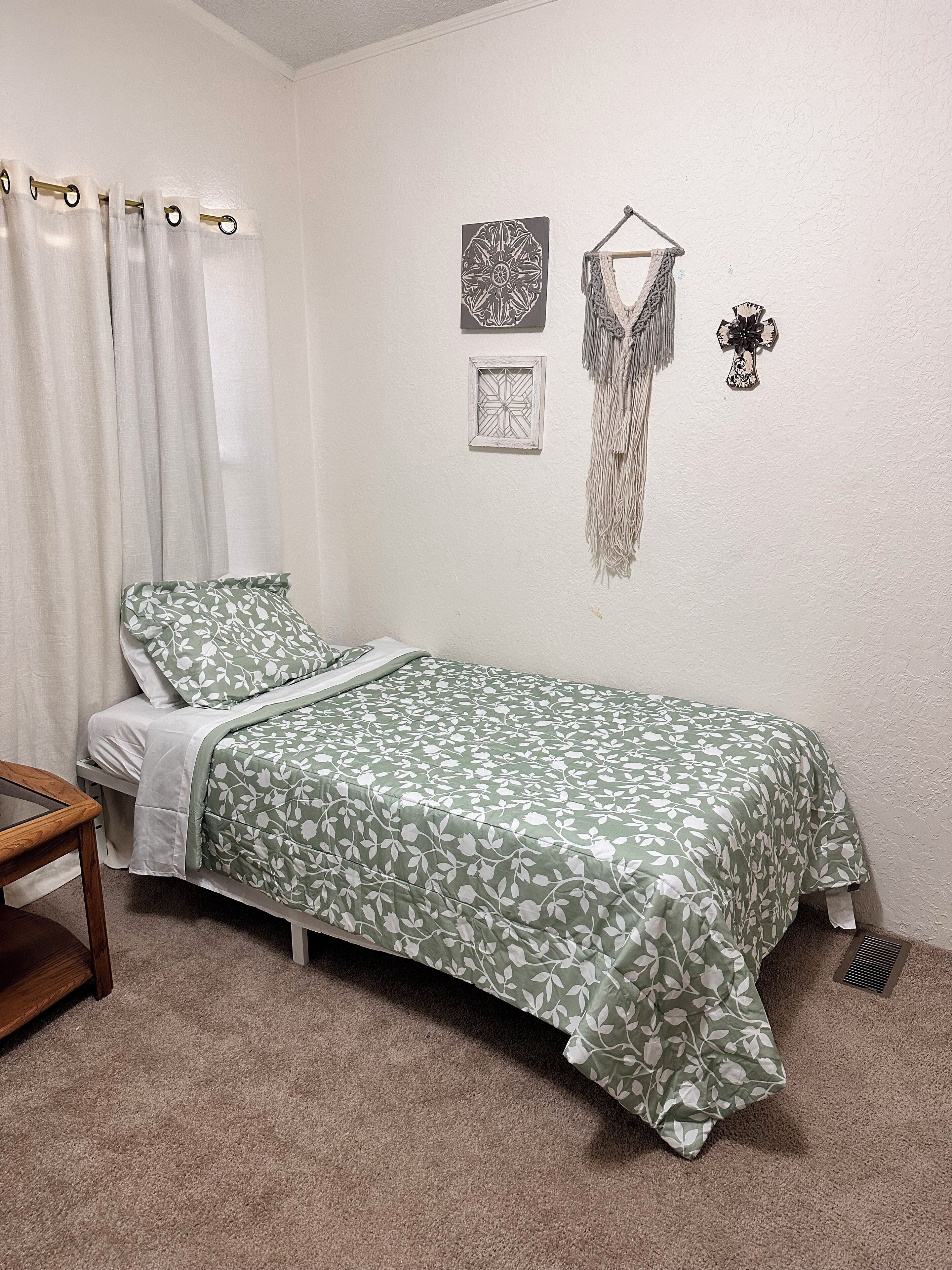 Un dormitorio con una cama, una mesita de noche de madera, un tapiz colgado y una cruz en la pared.
