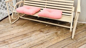 A wooden bench with two pink cushions on a wooden deck.