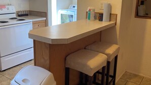 A kitchen with a central island, bar stools, a trash can, a stove, and a washing machine in the background.