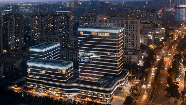 A modern high-rise building with multiple floors, featuring a prominent curved glass facade and illuminated signage. - Days Inn by Wyndham Hangzhou Gongshu (Hangzhou)