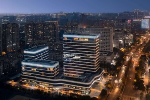 A modern high-rise building with multiple floors, featuring a prominent curved glass facade and illuminated signage.