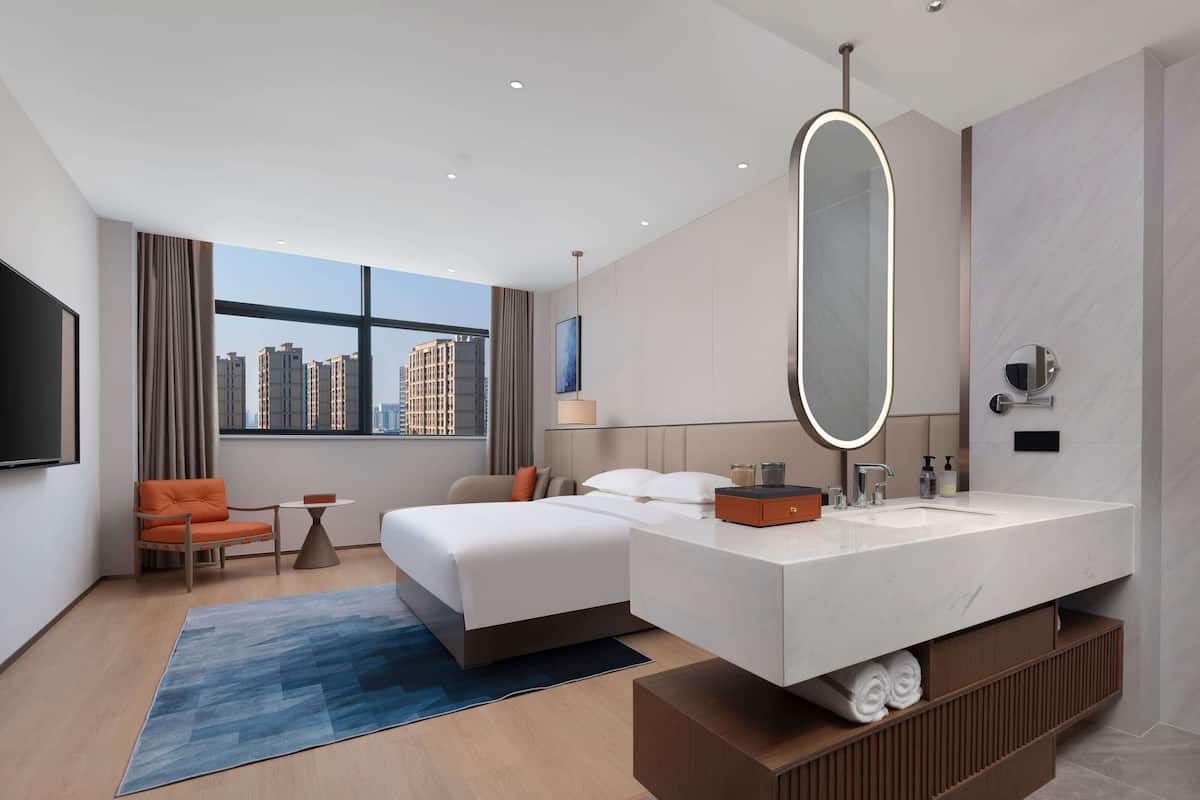 Une chambre d’hôtel moderne dotée d’un grand lit, d’une salle de bain avec un grand miroir, d’un bureau et offrant une vue sur la ville.