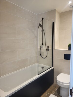 A modern bathroom with a glass-enclosed shower, a white bathtub, and a toilet.