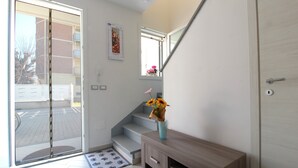 A modern hotel room with a sliding glass door leading to a balcony, a wooden console table with a vase of flowers, and a small window with a view of the outside. - Villetta Elena, Ac, Wifi, Lido Degli Scacchi (Comacchio)