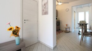 A hallway with a white door, a vase with sunflowers, a ceiling fan, and a dining area with a table and chairs. - Villetta Elena, Ac, Wifi, Lido Degli Scacchi (Comacchio)