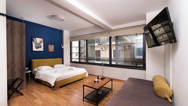 A modern hotel room with a bed, a sofa, a small table, and a TV mounted on the wall.