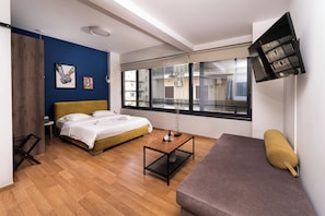 Quarto de hotel moderno com cama, sofá, mesinha e TV na parede.