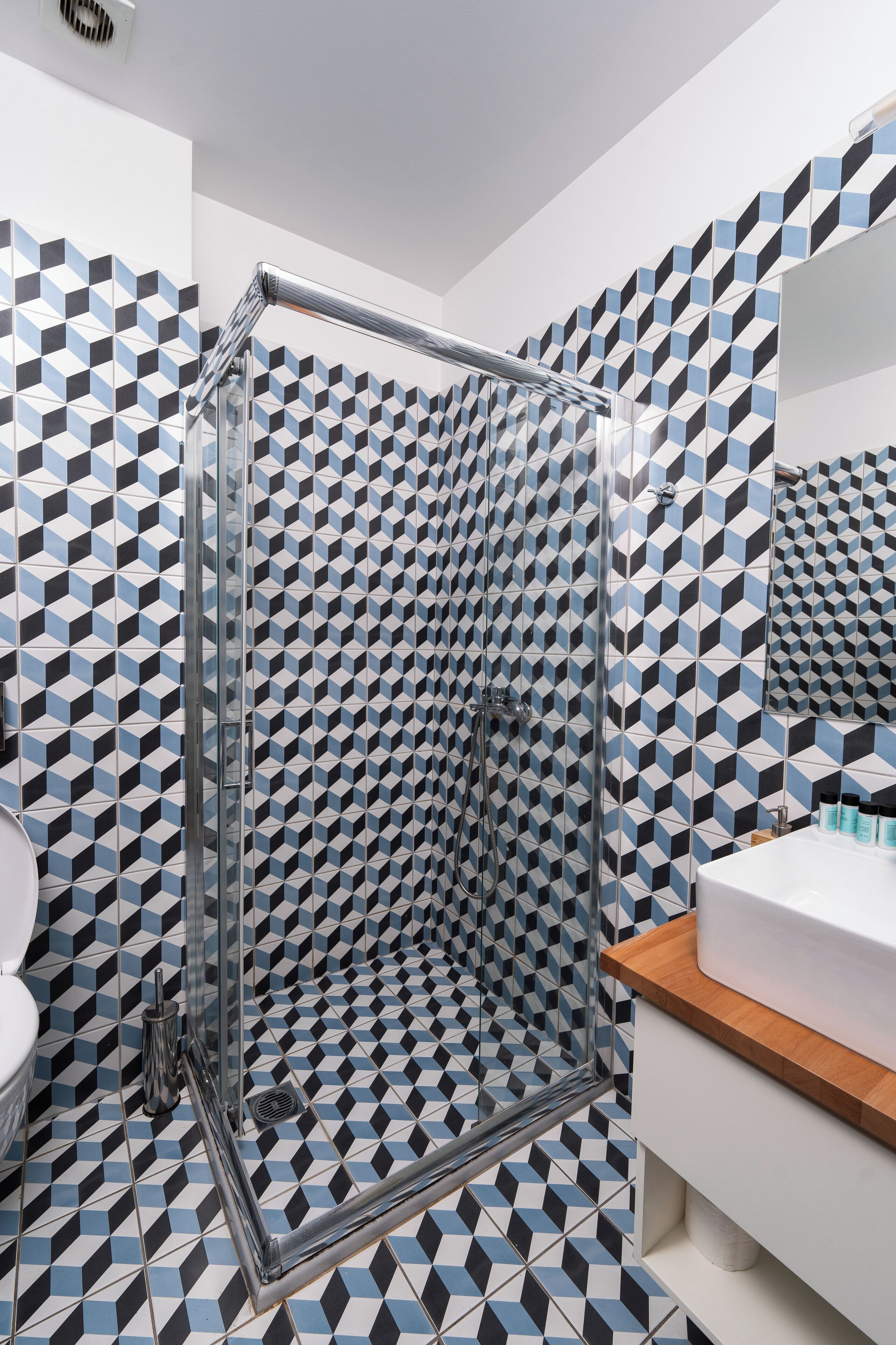 A bathroom with a geometric patterned tile floor and walls, a glass-enclosed shower, and a wooden countertop sink.
