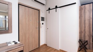 A room with a wooden door, a white closet with a sliding door, a small table with a remote control, and a wooden floor.