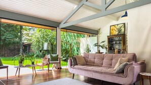 A spacious living area with a large window, a cushioned sofa, and a wooden coffee table. - Charme na Granja - Condomínio (Carapicuiba)