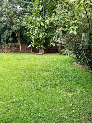 A grassy backyard with a stone wall, a wooden swing, and dense foliage.