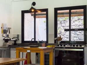 A kitchen with a stove, sink, and large windows. There are knives on the wall and a basket on the counter. - Charme na Granja - Condomínio (Carapicuiba)