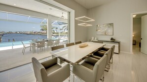 Un comedor moderno con una gran mesa de vidrio y sillas, con vista a una piscina y al agua.