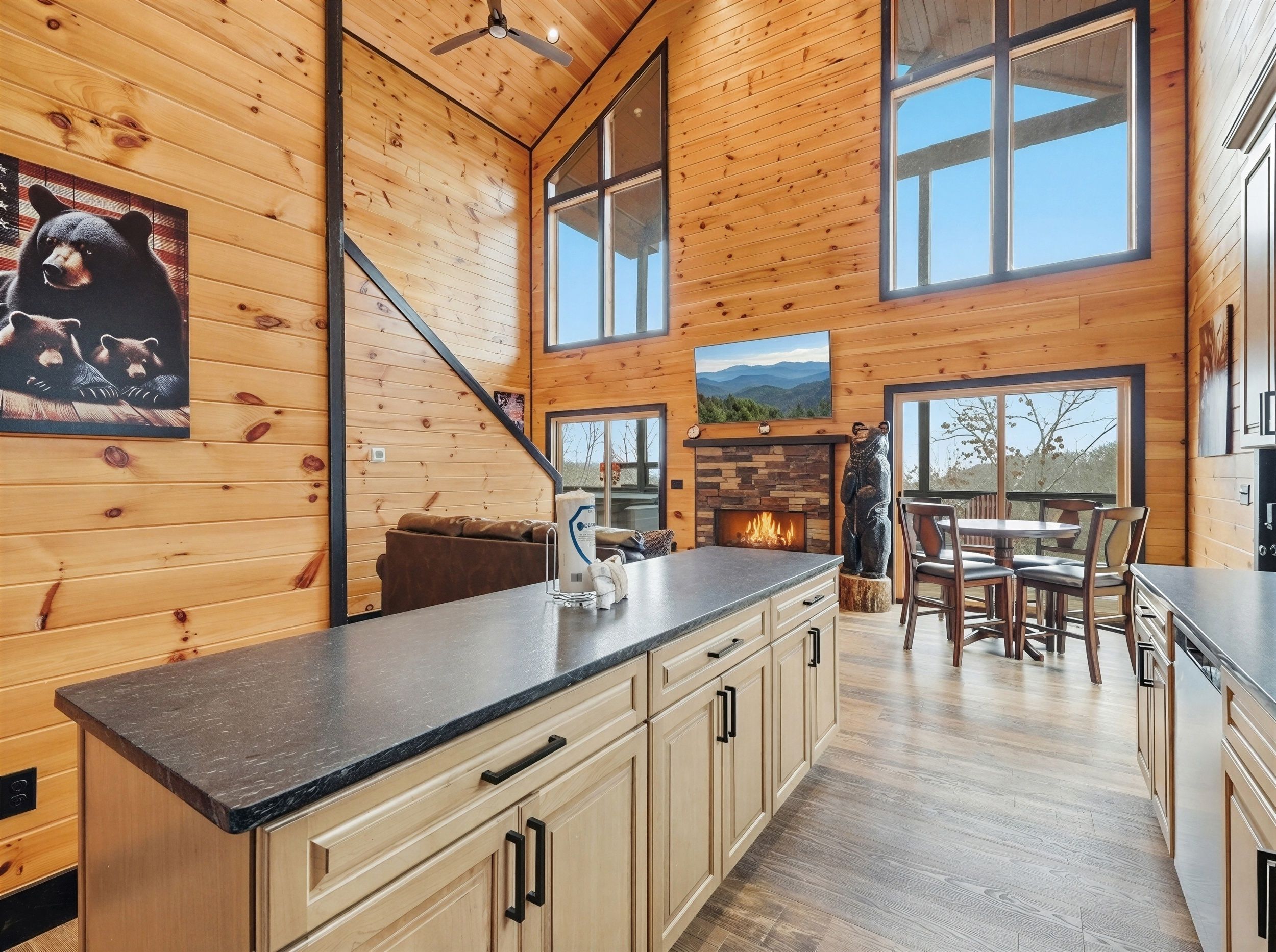 A cabin interior with wooden walls, a fireplace, a dining area, and a kitchen with a granite countertop.