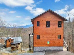 Eine Holzhütte mit Balkon, einer Treppe und Blick auf den umliegenden Wald und die Berge.