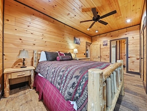 Un dormitorio de cabaña de madera con cama, mesita de noche, lámpara y ventilador de techo.