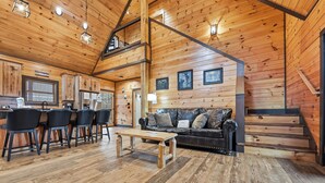 A cozy cabin interior with a wooden interior, a dining area with chairs, a sofa, and a staircase.