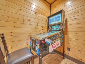 A wooden-paneled room with a pinball machine and a single chair.