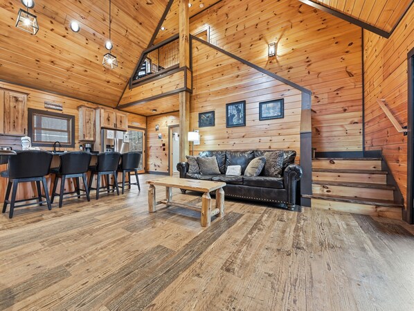 A cozy cabin interior with a wooden interior, a dining area with chairs, a sofa, and a staircase.