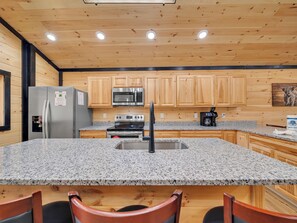 Une cuisine dotée de plans de travail en granit, de meubles en bois, d’appareils électroménagers en acier inoxydable et d’un robinet noir.