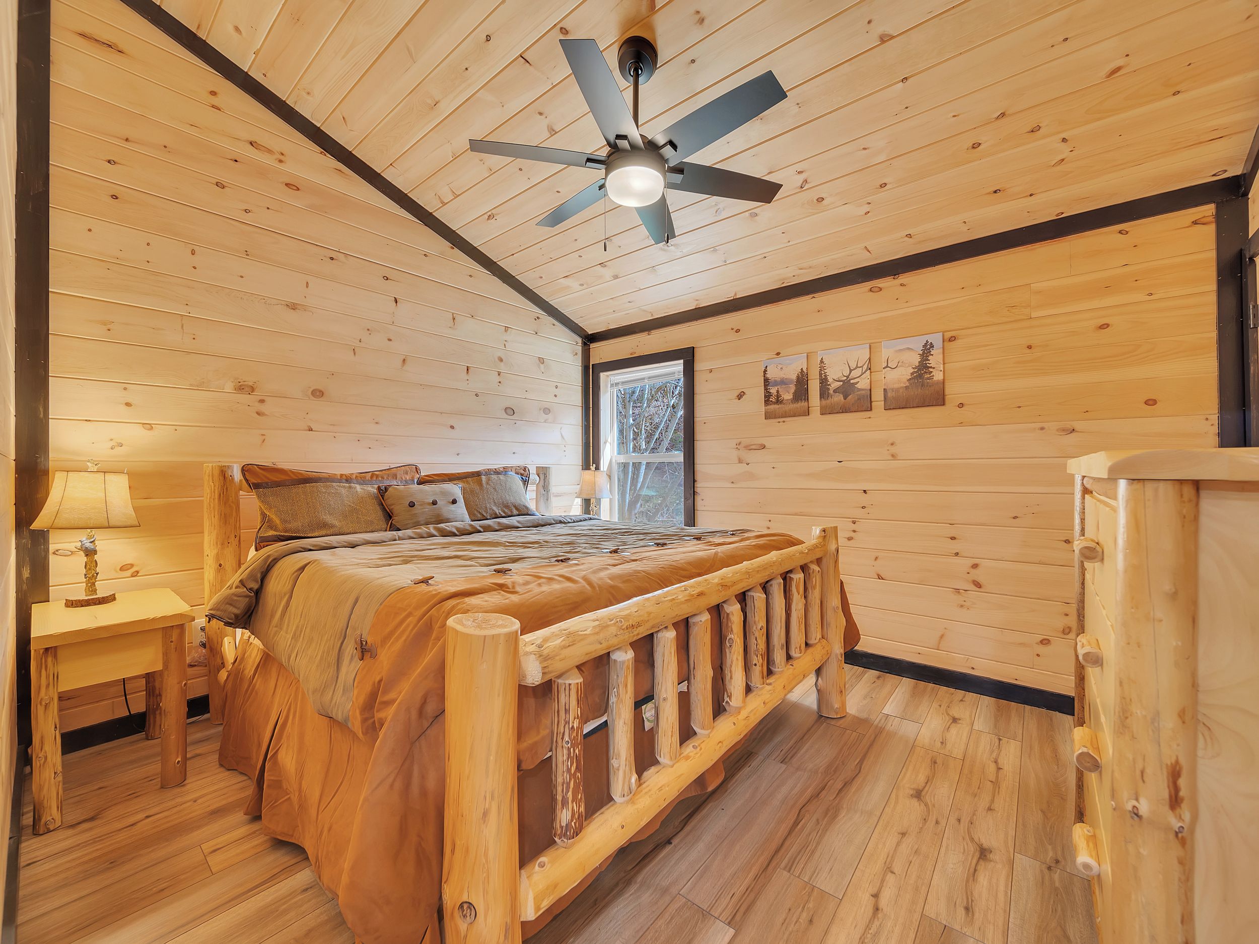 Ein Schlafzimmer einer Holzhütte mit Bett, Nachttisch, Lampe, Deckenventilator und Holzkommode.