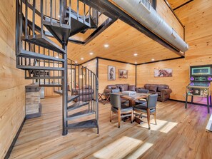 Un intérieur en bois avec un escalier en colimaçon, un espace de vie comprenant un canapé et des fauteuils, ainsi qu’une console de jeux.