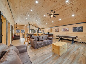 A spacious room with wooden walls and ceiling, a brown leather sofa, a pool table, and a dining area with chairs and a table. - Luxury Cabin w/Huge Game Room, Fire Pit & Hot Tub (Pigeon Forge)