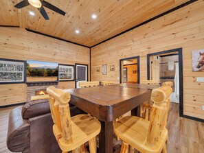 A wooden interior with a large dining table and chairs, a fireplace, and a ceiling fan. - Luxury Cabin w/Huge Game Room, Fire Pit & Hot Tub (Pigeon Forge)