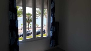 A room with a window overlooking a beach with palm trees and parked cars. - Alpes maritimes front de mer cagnes sur mer  (Cagnes-sur-Mer)