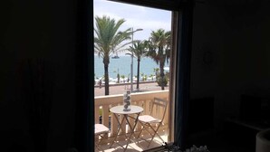 A balcony with a table and chairs, overlooking a beach with palm trees and a boat in the distance. - Alpes maritimes front de mer cagnes sur mer  (Cagnes-sur-Mer)