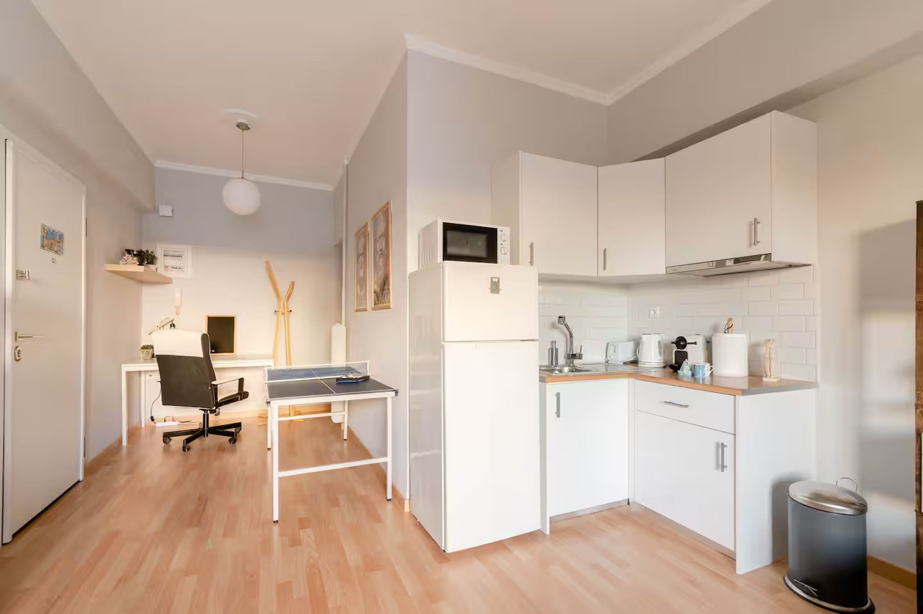 A compact kitchen with white cabinets, a microwave, a sink, and a trash bin.