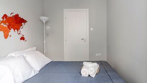 A bedroom with a bed, white pillows, a folded towel on the bed, a white lamp, and a white door. - Athenian Entertainment Relaxation Hub (Athens)