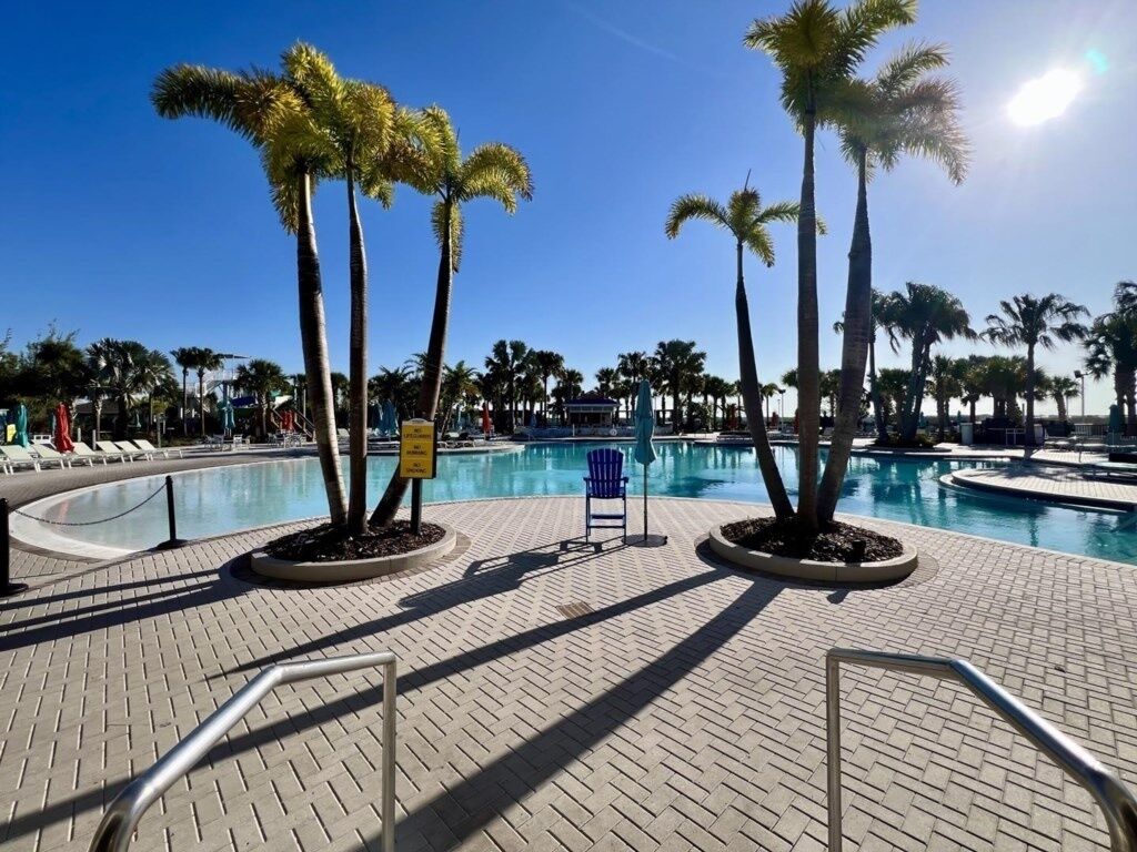 A pool area with palm trees, lounge chairs, and a clear sky.
