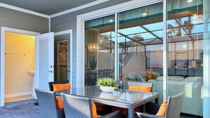 Un espace patio aménagé avec une table à plateau de verre, des chaises en osier et une plante en pot.