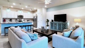 Une cuisine moderne dotée d’un îlot central, d’un coin repas avec une table basse de couleur sombre et de deux canapés recouverts d’un tissu bleu clair.
