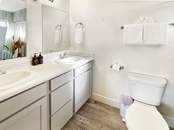A modern bathroom with a white sink, mirror, and toilet. There are two towels hanging on the wall and a trash can next to the toilet. - Bark And Bike Abode 3 Bedroom Home (Fruita)
