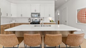 A modern kitchen with white cabinets, a central island with seating, a stove, and a microwave. - Villa #30 At Bloomington Country Club - Red Cliffs 4 Bedroom Townhouse (St. George)
