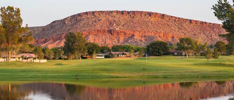 A tranquil golf course with a clear reflection in the water, surrounded by trees and a mountain in the background.