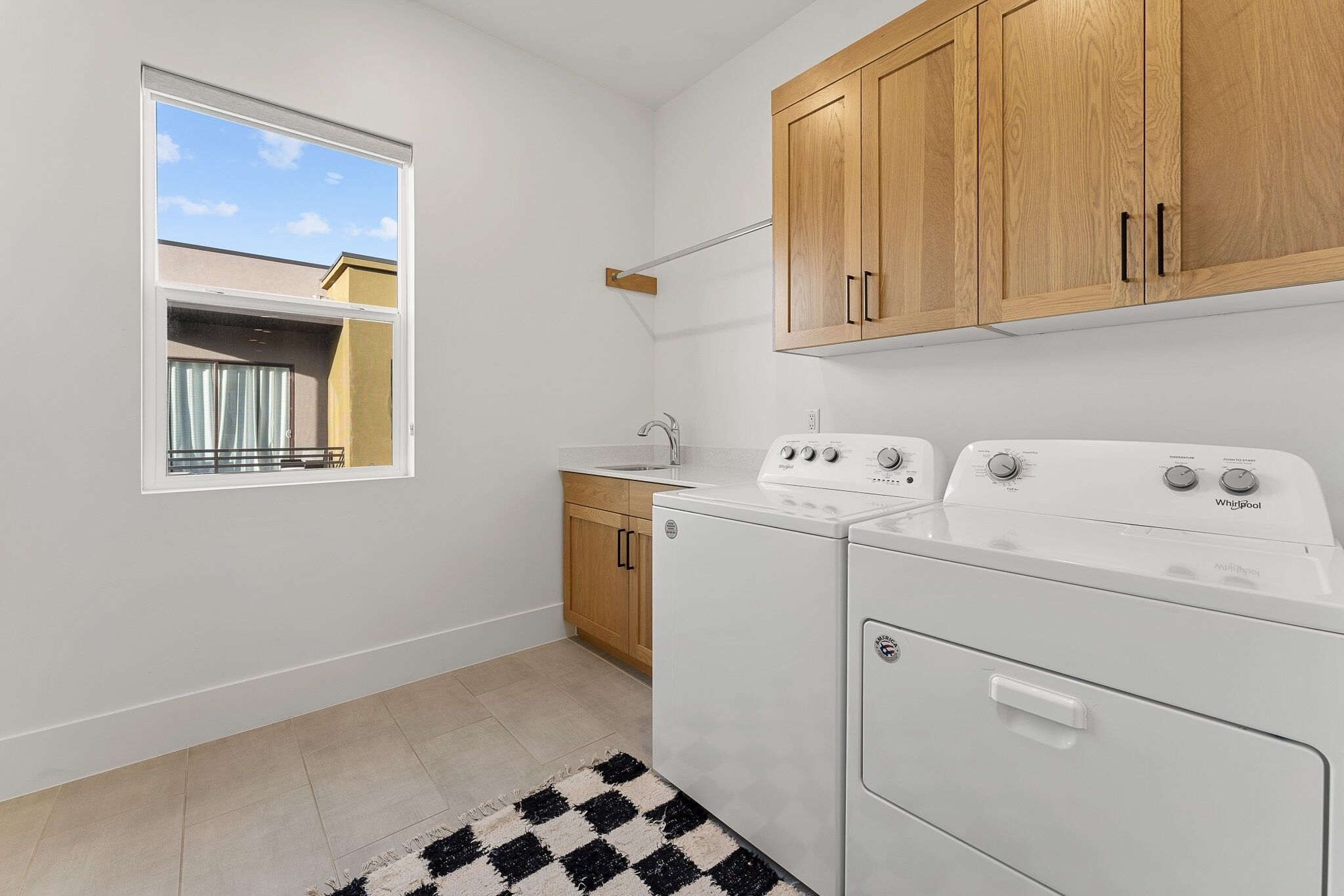 A laundry room with a washer and dryer, wooden cabinets, a window, and a view of a balcony.