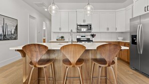 A modern kitchen with white cabinets, stainless steel appliances, and wooden bar stools. - Villa #11 Adventure Retreat At Bloomington Villas 4 Bedroom Townhouse (St. George)