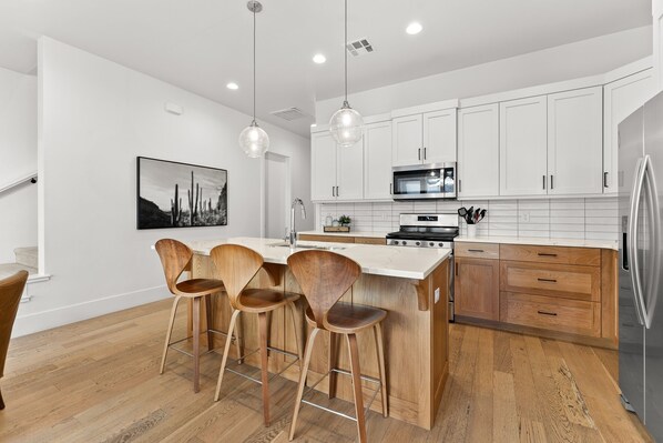 A modern kitchen with white cabinets, a central island with bar stools, stainless steel appliances, and pendant lighting. - Villa #11 Adventure Retreat At Bloomington Villas 4 Bedroom Townhouse (St. George)