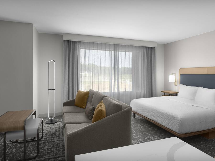 A hotel room with a bed, a sofa, a small table, and a floor lamp.