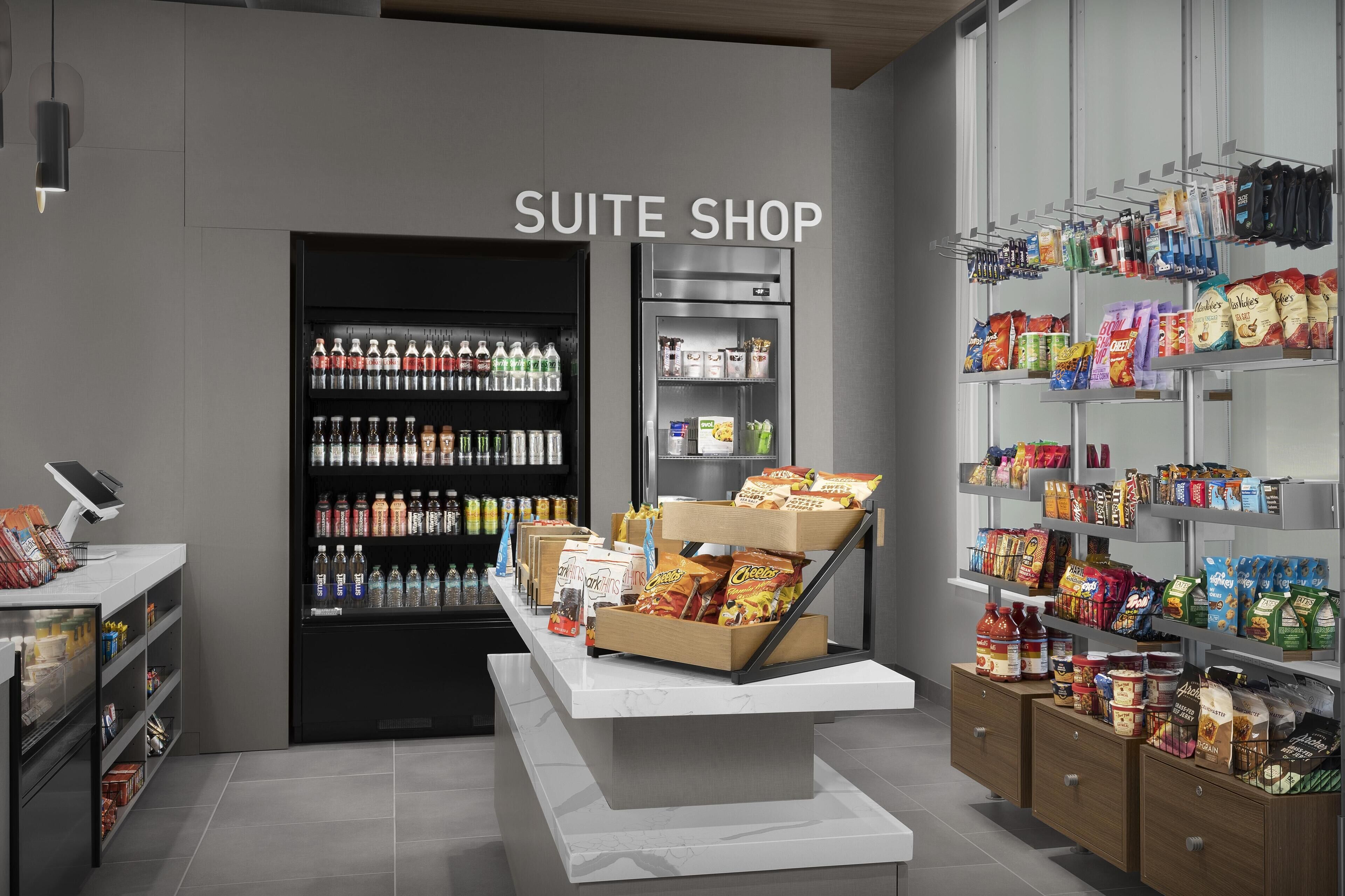 A suite shop with a refrigerated display, snack and beverage shelves, and a checkout counter.